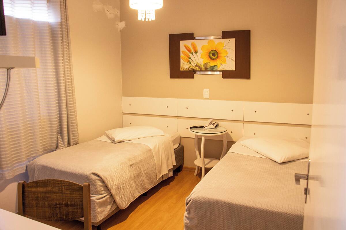 A hotel room with two single beds, a small round table, and a wall-mounted mirror.