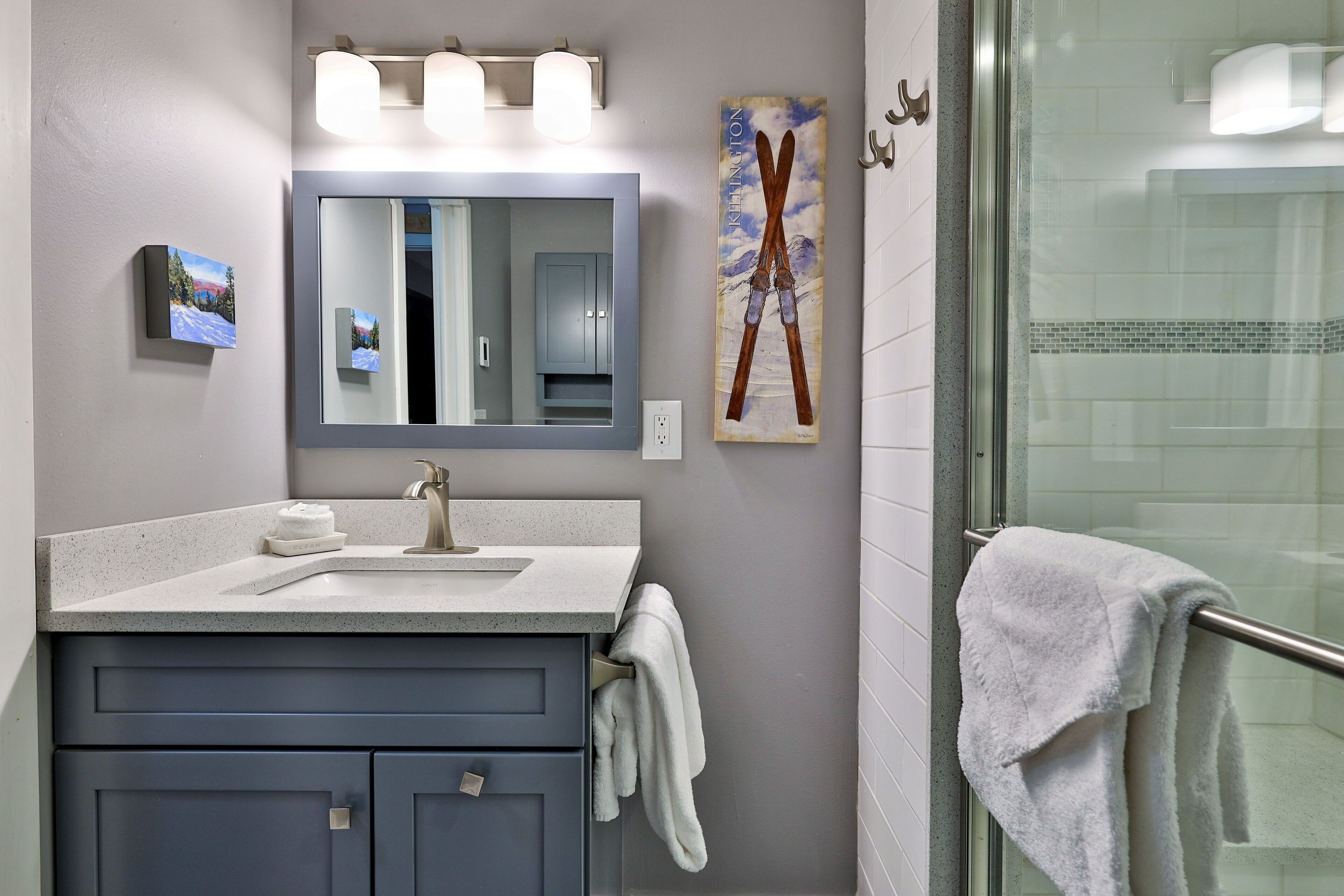 A bathroom with a large mirror, a sink, and a glass shower enclosure.