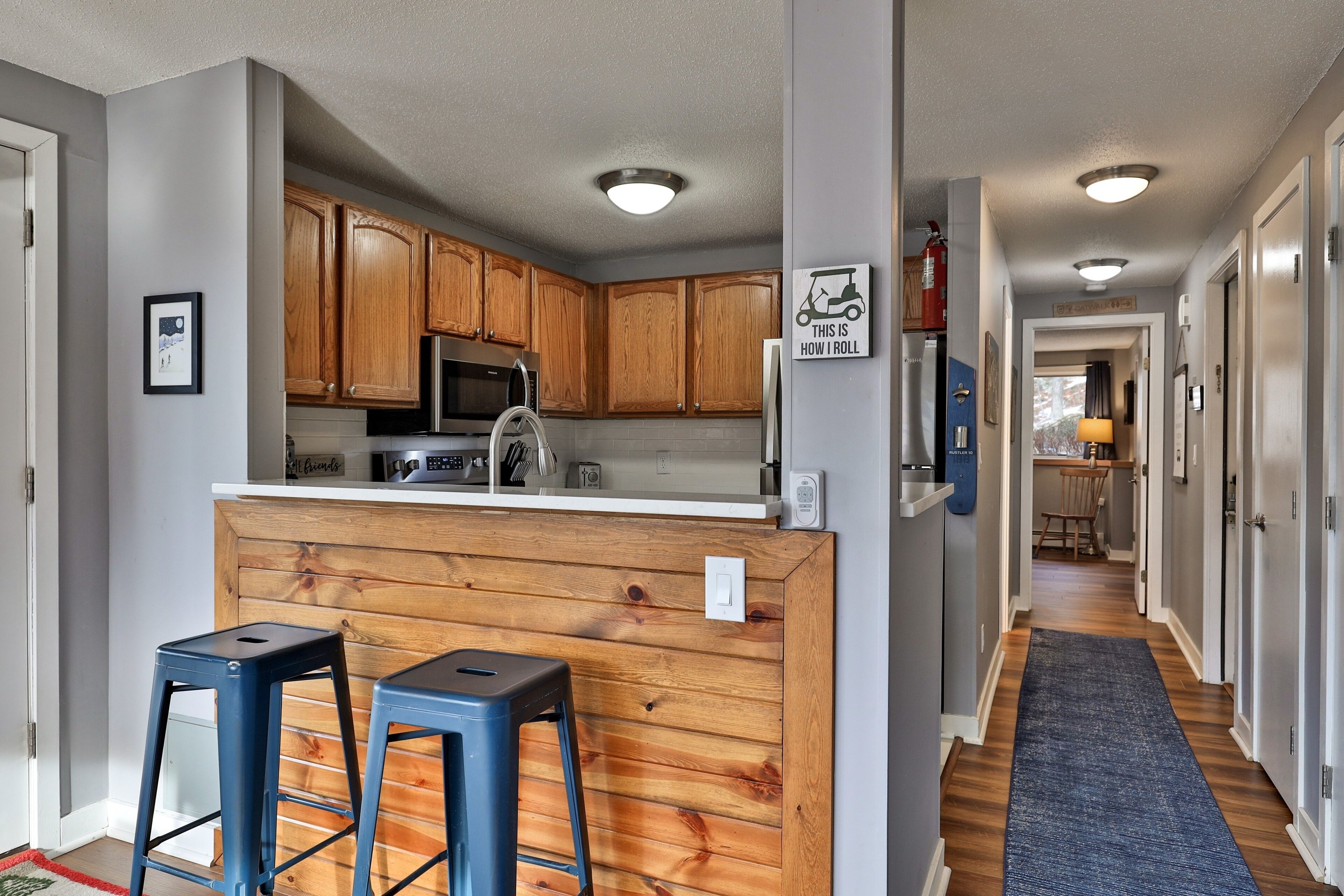 A modern kitchen with wooden cabinets, a central island, and two blue bar stools.