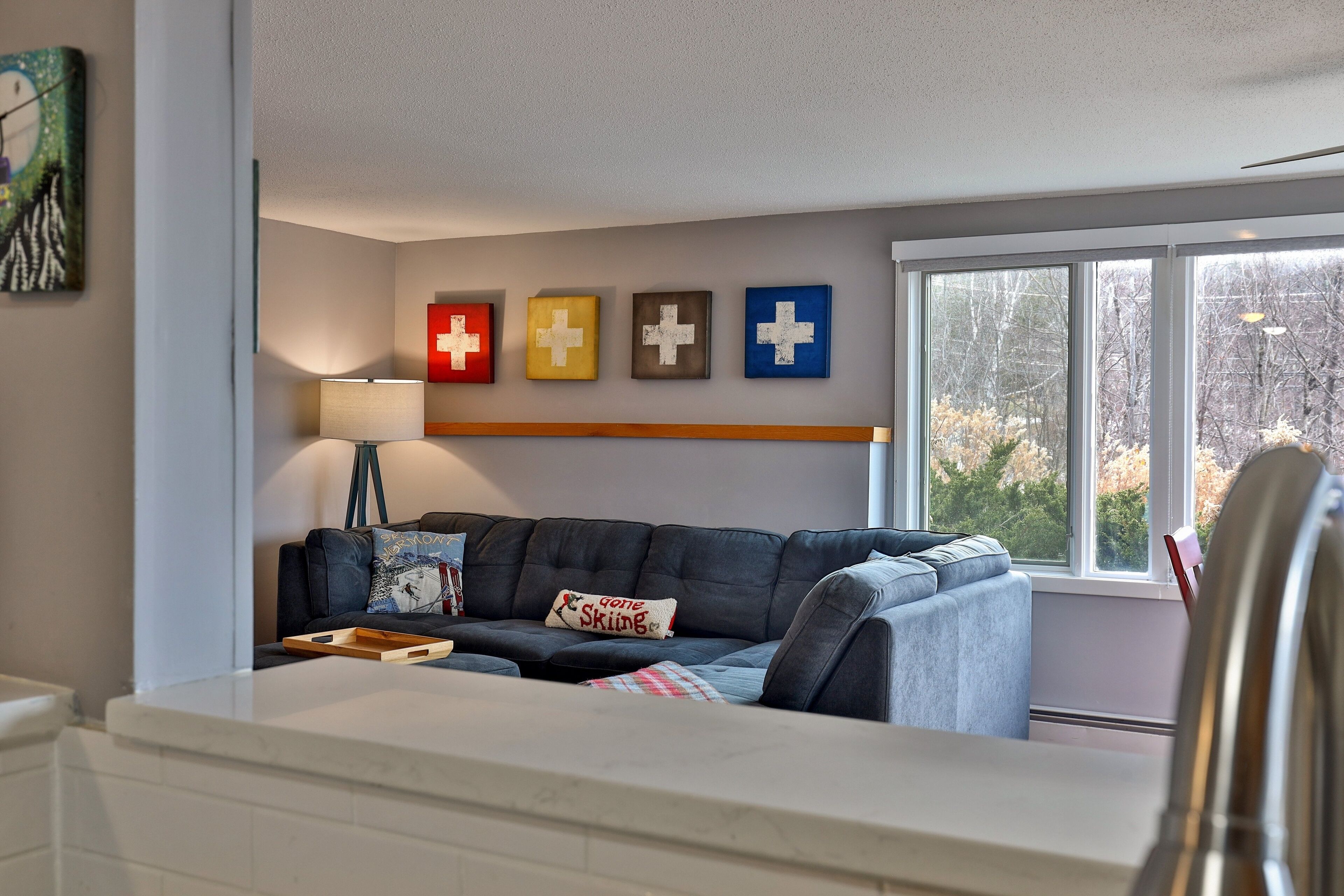 A living room with a dark grey sofa, a wooden shelf, and a window with a view of trees.