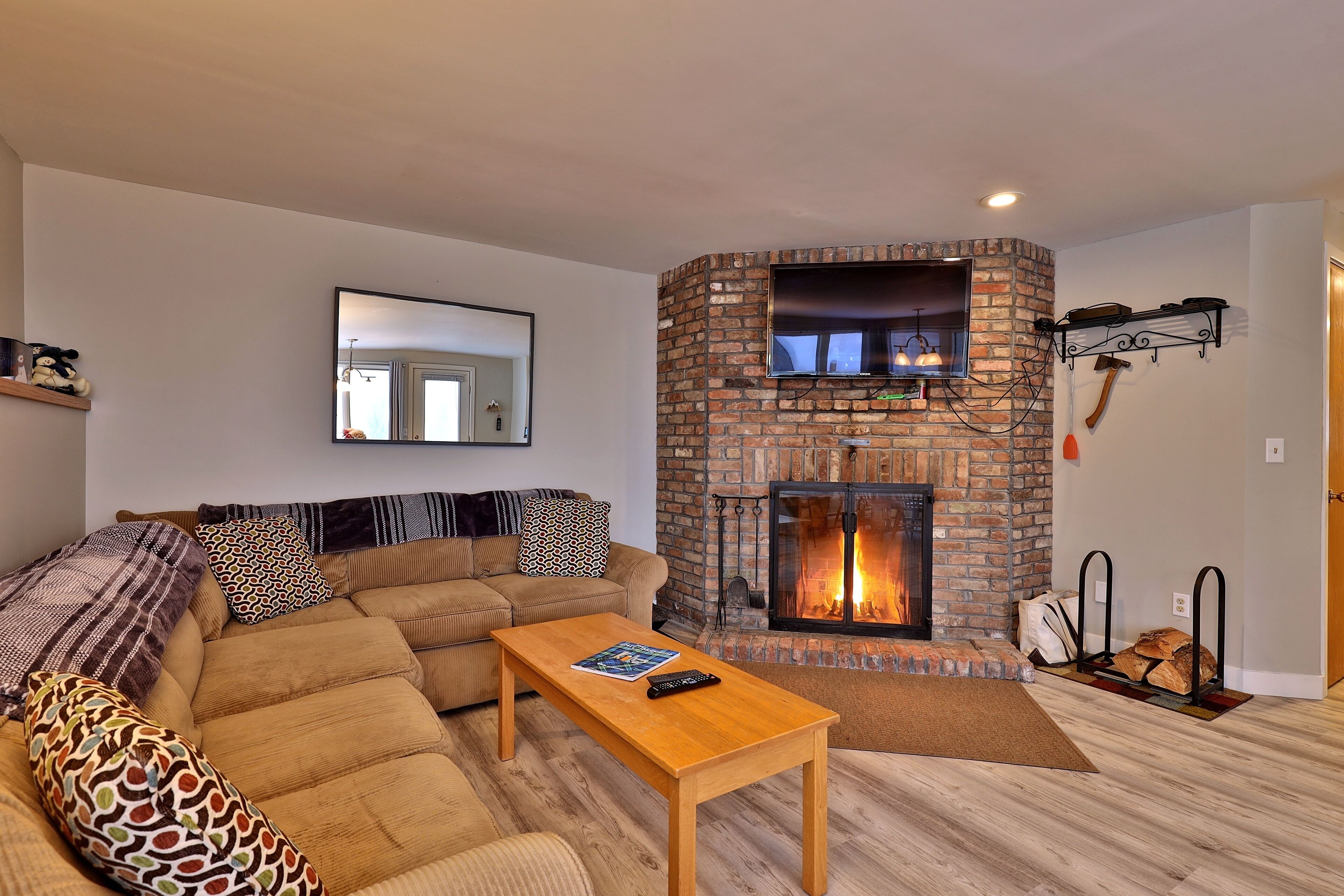 A living room with a brick fireplace, a sofa, a coffee table, and a television mounted on the wall.