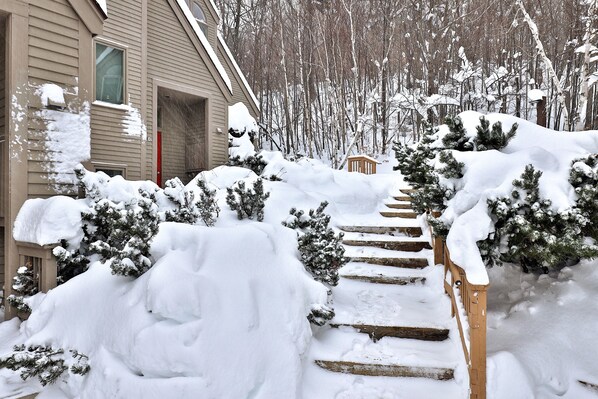 A snow-covered outdoor area with a wooden staircase leading up to a house.