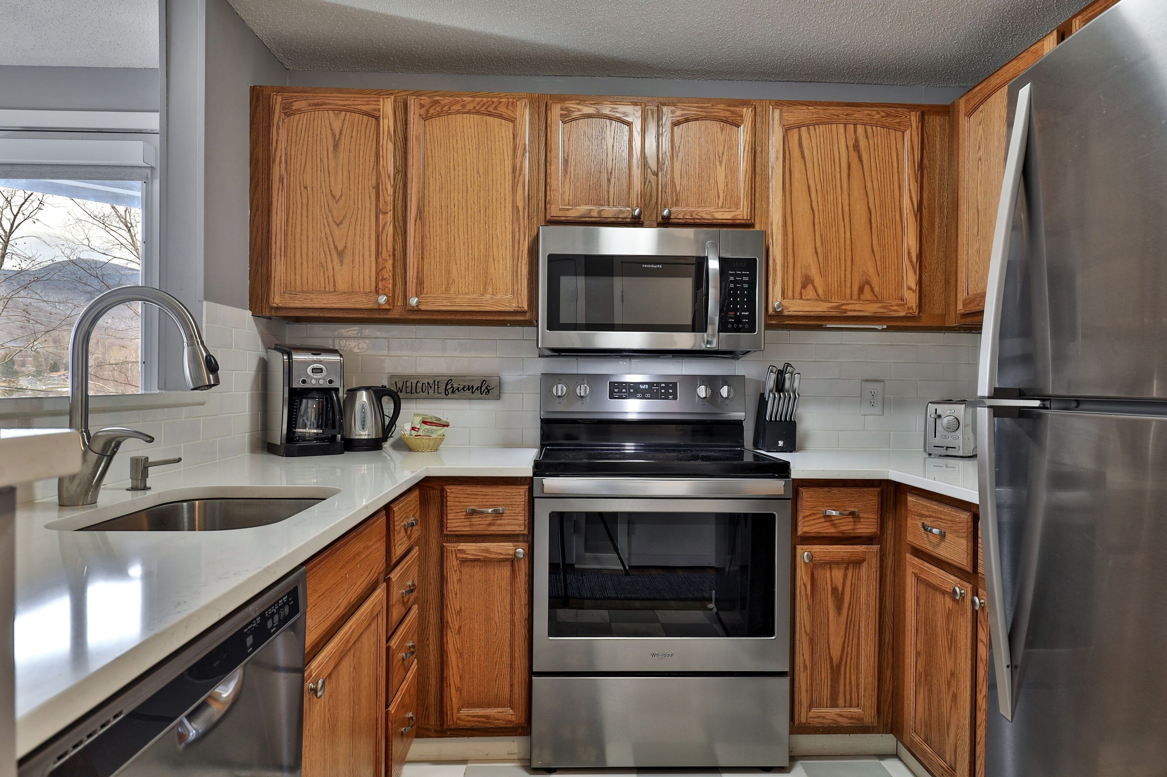A modern kitchen with wooden cabinets, stainless steel appliances including a microwave, oven, and refrigerator, a dishwasher, and a coffee maker.