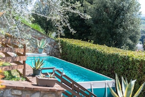A swimming pool with a wooden deck, potted plants, and a stone wall.