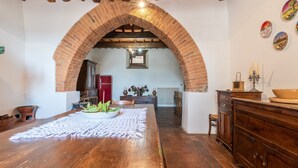 Ein rustikales Interieur mit einem Holzespeisetisch, einem Ziegelbogen und einer durch den Bogen sichtbaren Küche.