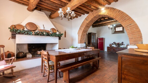 Eine rustikale Küche mit Holztisch, Bänken, Kamin und Ziegelgewölben.