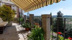 Ein Balkon mit gestreiftem Jalousievorhang, Blumentöpfen und Blick auf die Landschaft.