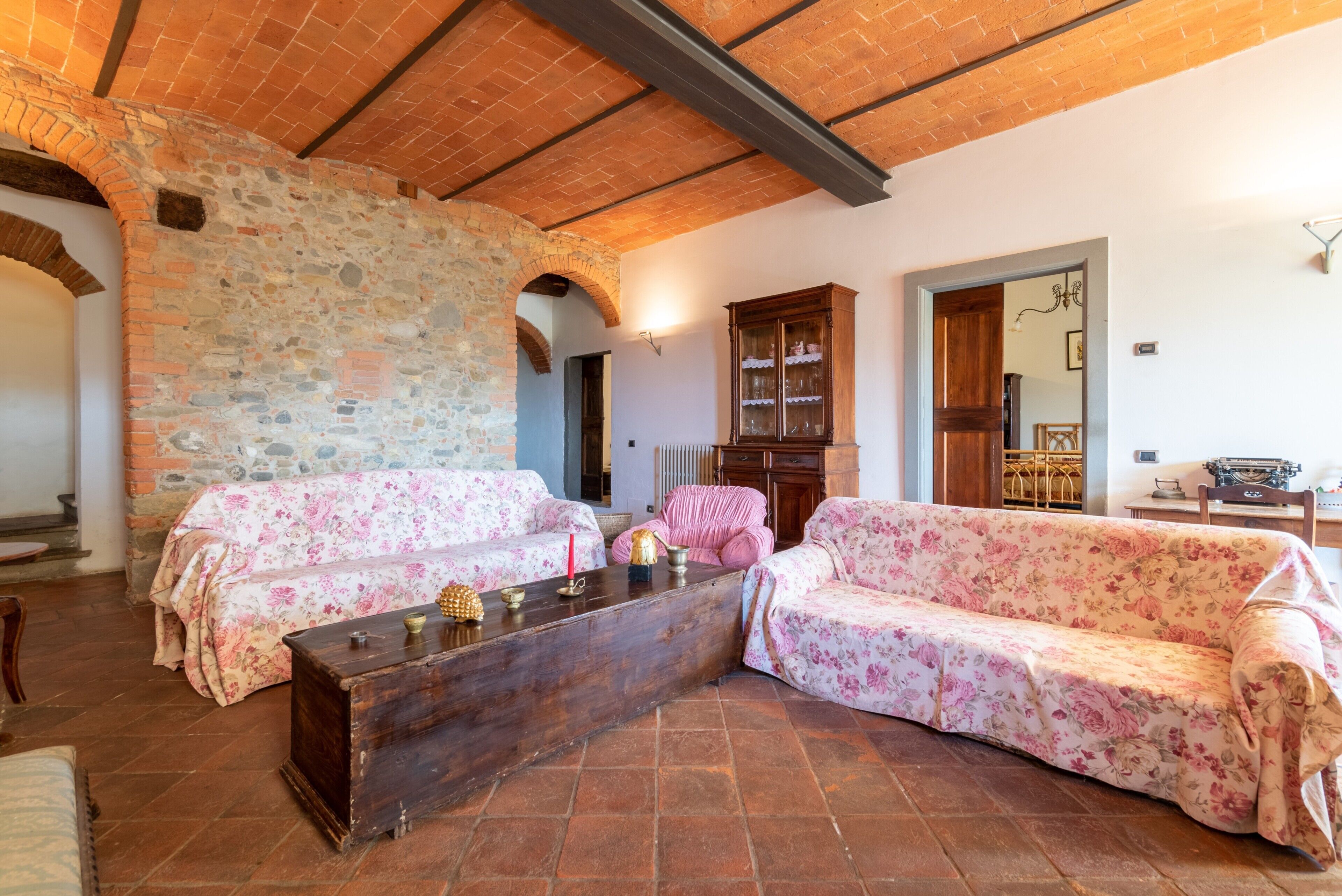 Ein Zimmer mit Steinwänden, Holzboden und floralen Sofas sowie einem Holztisch.