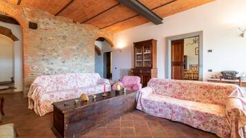 Ein Zimmer mit Steinwänden, Holzboden und floralen Sofas sowie einem Holztisch.