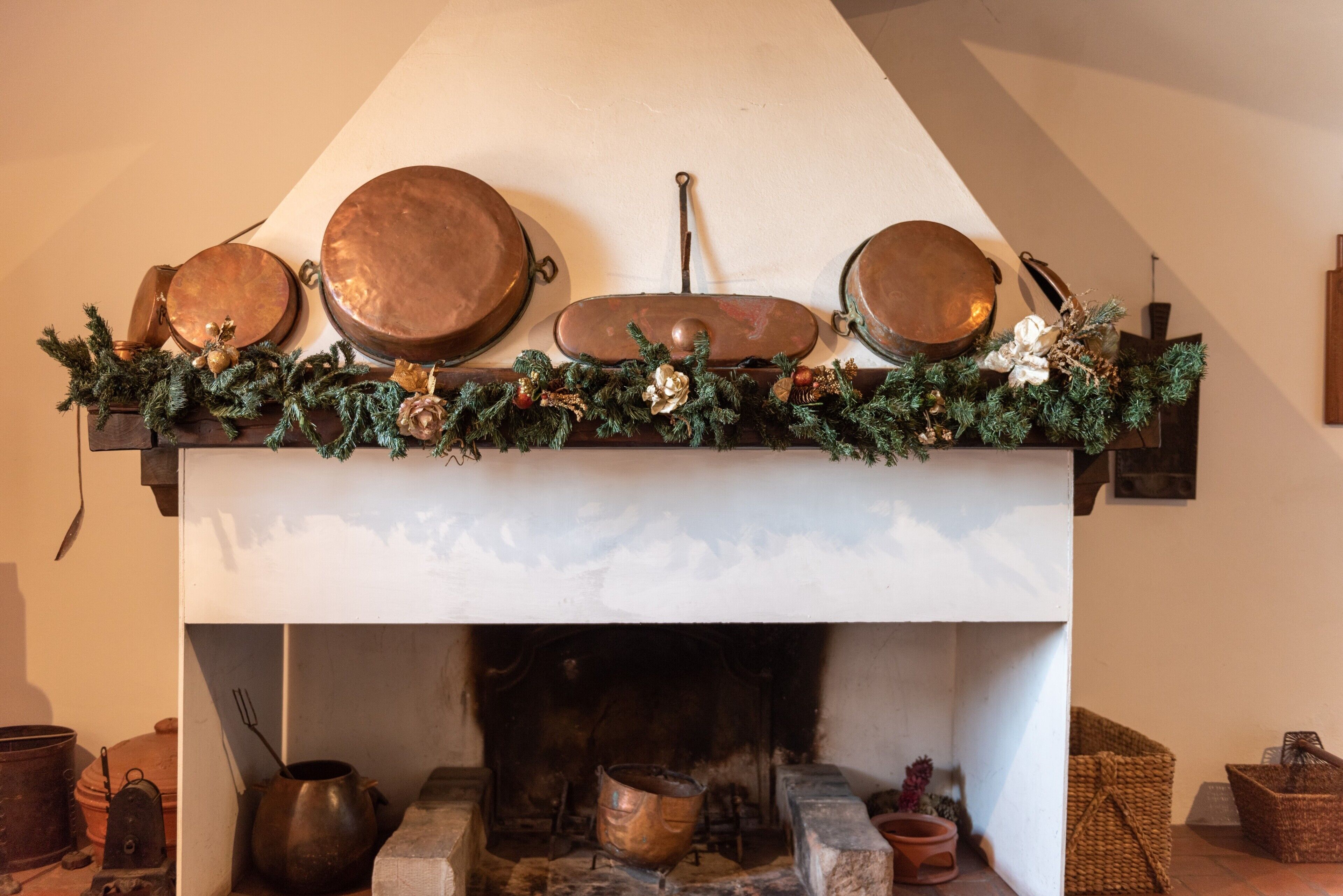 Une cheminée surmontée d’une étagère où sont disposés des pots en cuivre, une guirlande décorative et une cheminée en pierre rustique.