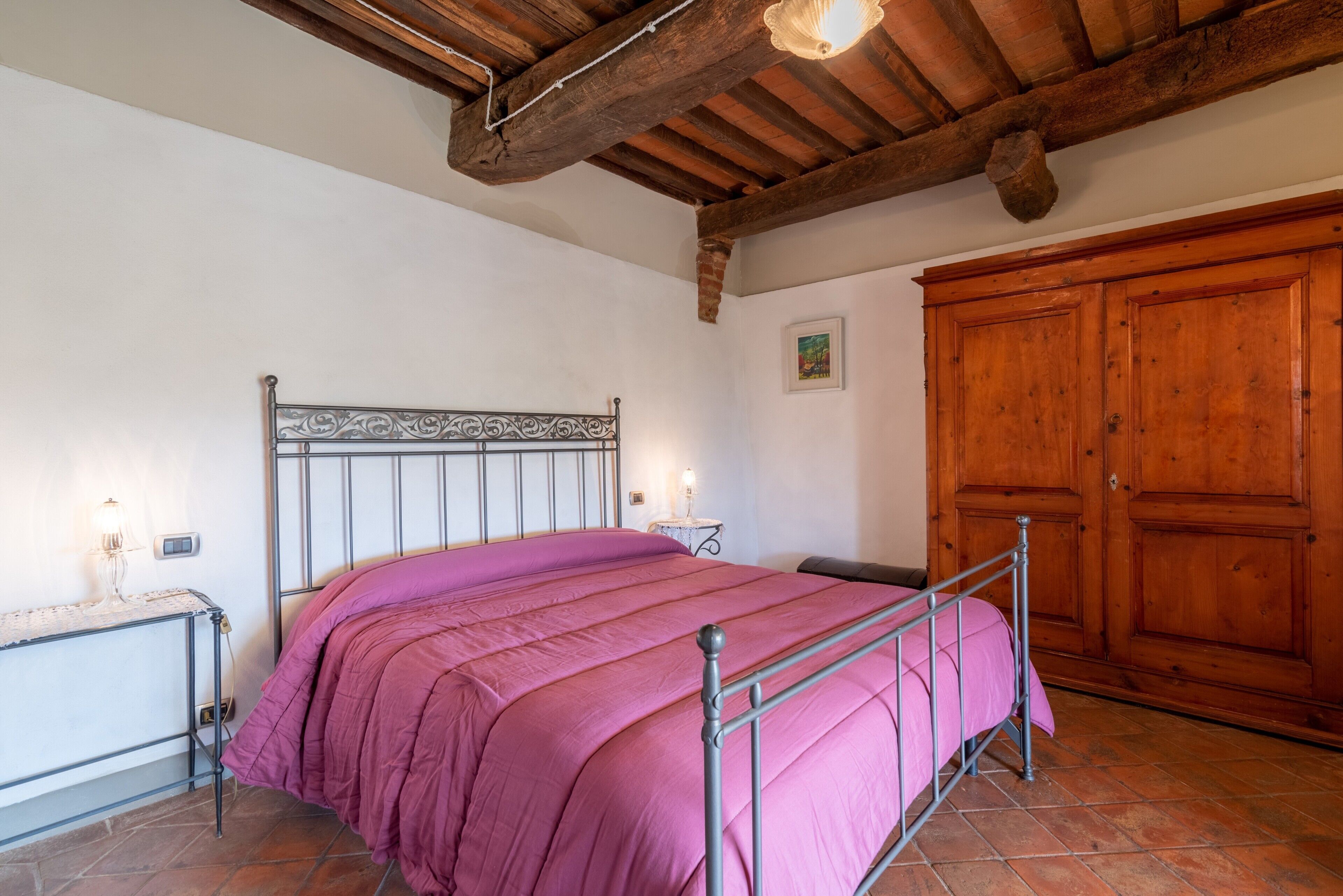 A bedroom with a metal bed frame, a wooden wardrobe, and a tiled floor.