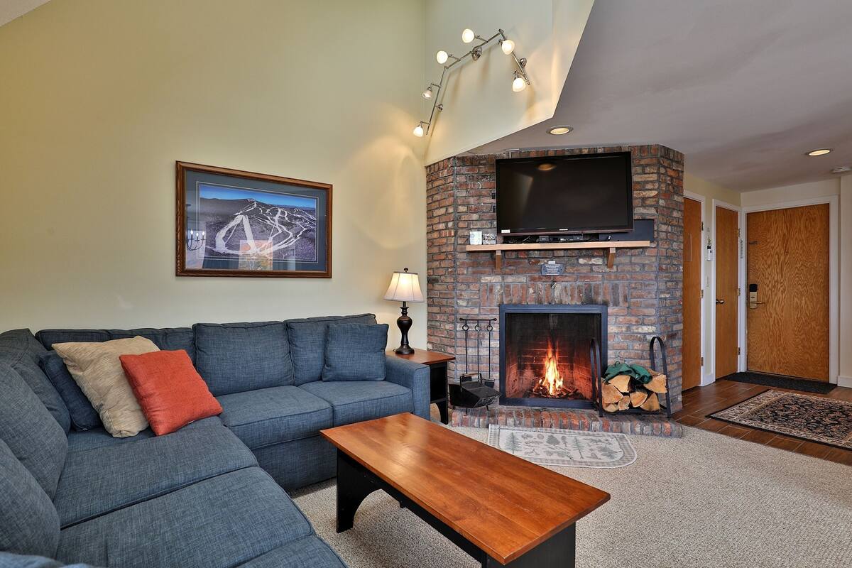 A living room with a sectional sofa, a wooden coffee table, a fireplace, and a mounted TV.