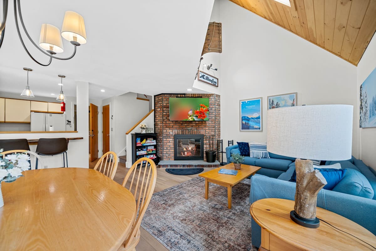 A cozy living room with a fireplace, a dining area, and a kitchen.