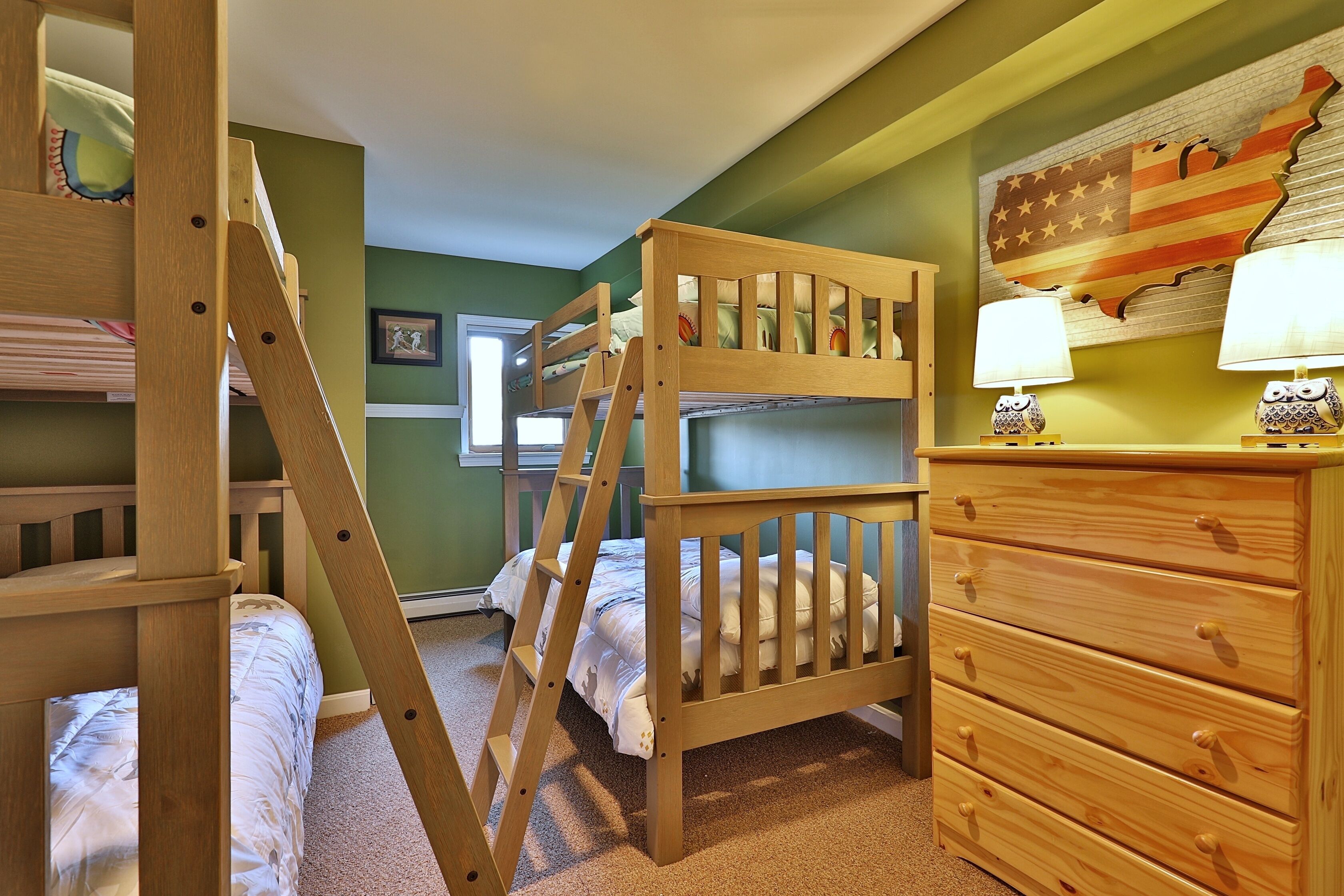 Une chambre avec un lit superposé, une échelle en bois, une commode à tiroirs et un mur décoré d’une carte.