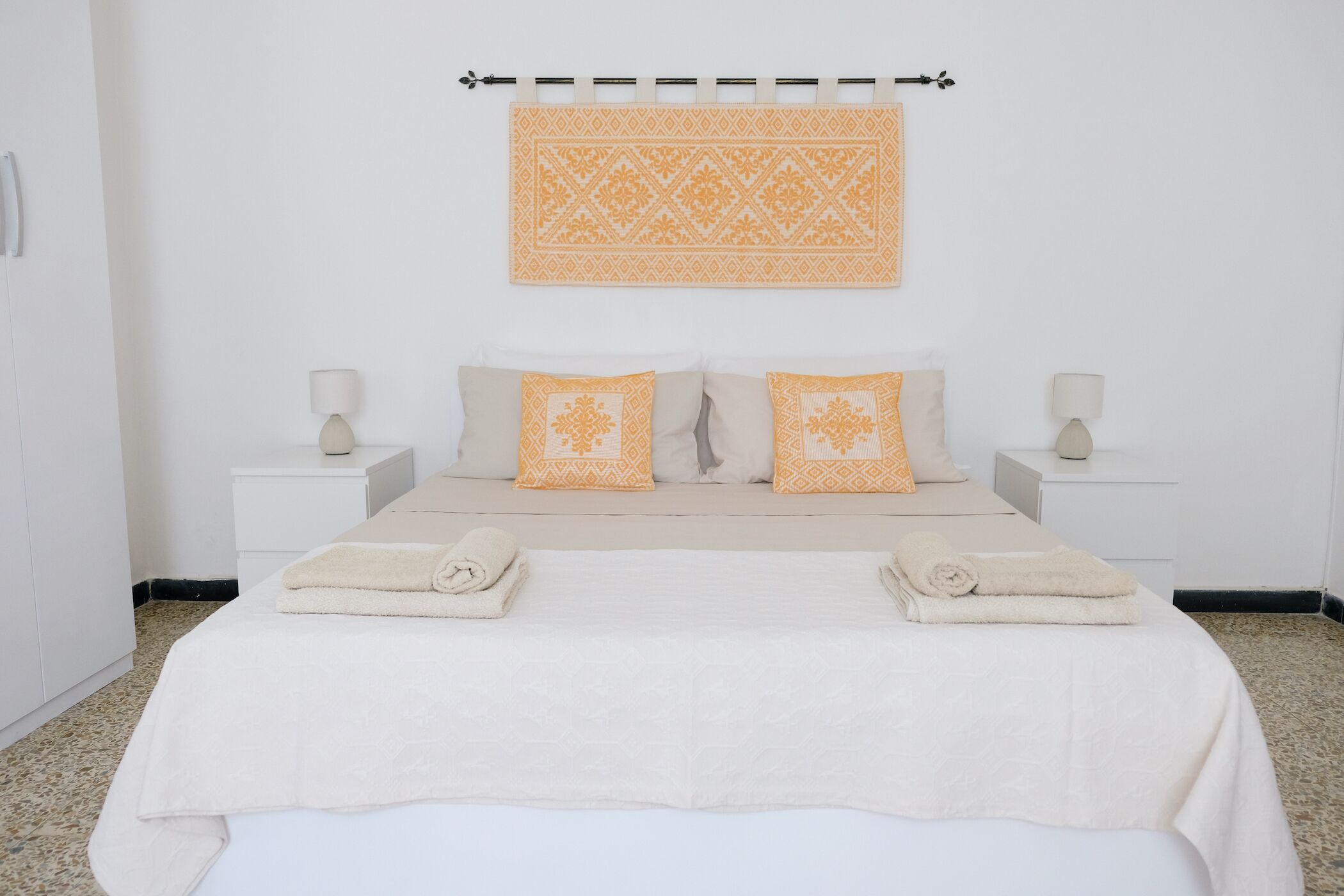 Une chambre à coucher bien rangée, avec un lit, deux tables de chevet et un élément décoratif fixé au mur.