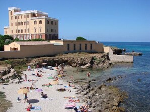 Un hotel sulla costa con un edificio ampio, una spiaggia sabbiosa e acque blu cristalline.