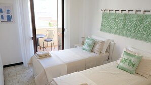 Hotellihuone, jossa on kaksi sänkyä, pieni pöytä, tuoli ja näkymä ulos.
