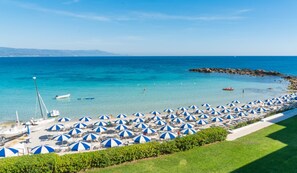 A beach with numerous blue and white striped umbrellas, boats, and a clear view of the sea. - Just 80 meters from the sea, Best area of Alghero, 3 bedrooms+private parking+AC (Alghero)