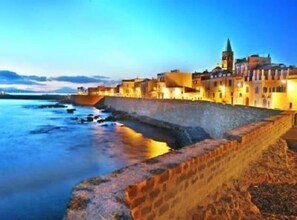 A coastal town with a prominent church tower, a fortified wall, and buildings along the waterfront. - Just 80 meters from the sea, Best area of Alghero, 3 bedrooms+private parking+AC (Alghero)