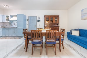 A dining area with a wooden table and chairs, a kitchen with blue cabinets, and a blue sofa in a living room.