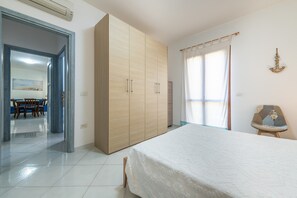 A bedroom with a bed, wardrobe, and a dining area visible through an open door. - Holiday Home 'Casa Celeste' with Shared Pool, Private Terrace and Air Conditioning (Villasimius)