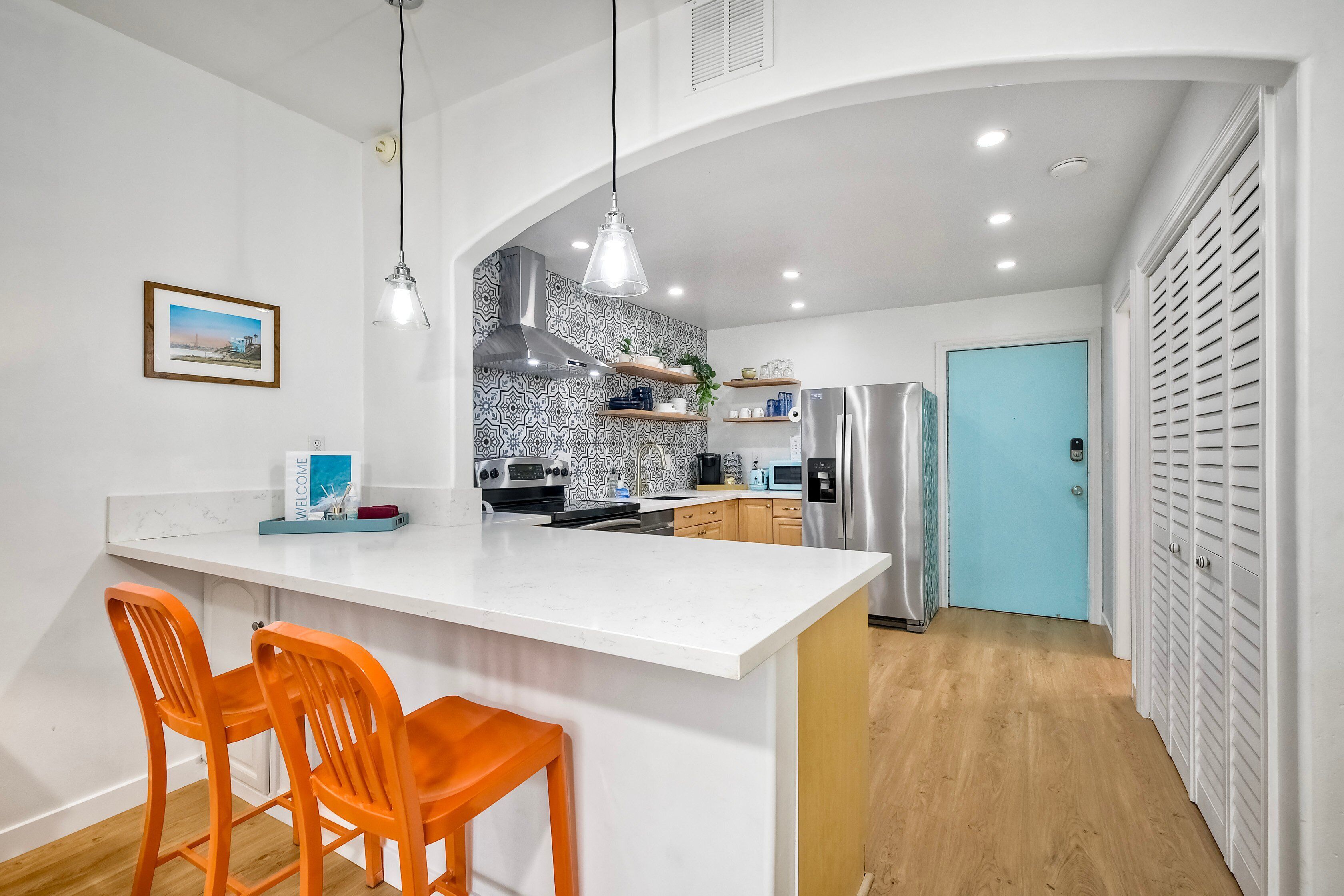 Una cucina moderna con un'isola bianca, sedie arancioni e una porta blu.