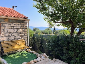 A stone building with a red-tiled roof, a wooden bench, and a view of mountains.