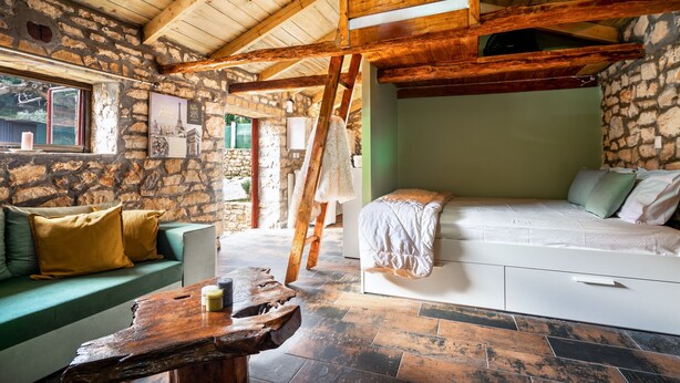 A rustic room with stone walls, a wooden ceiling, a bed, a sofa, and a table. - Villa 'Nikos' with Mountain View, Wi-Fi and Air Conditioning (KEFALONIA)