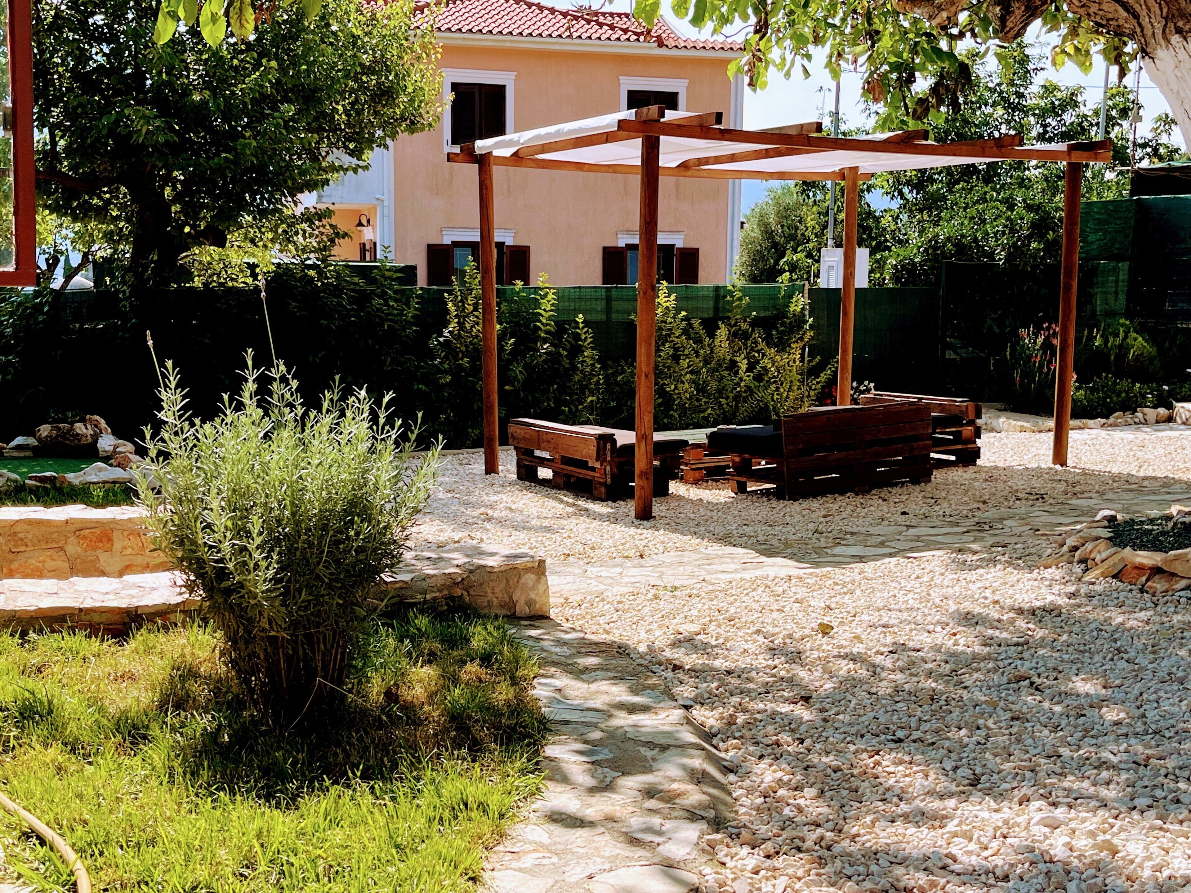 A covered outdoor seating area with benches, surrounded by gravel and greenery.