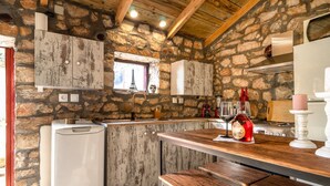 Una cocina rústica con paredes de piedra, vigas de madera, un banco empotrado y una ventana con vistas a la Torre Eiffel.