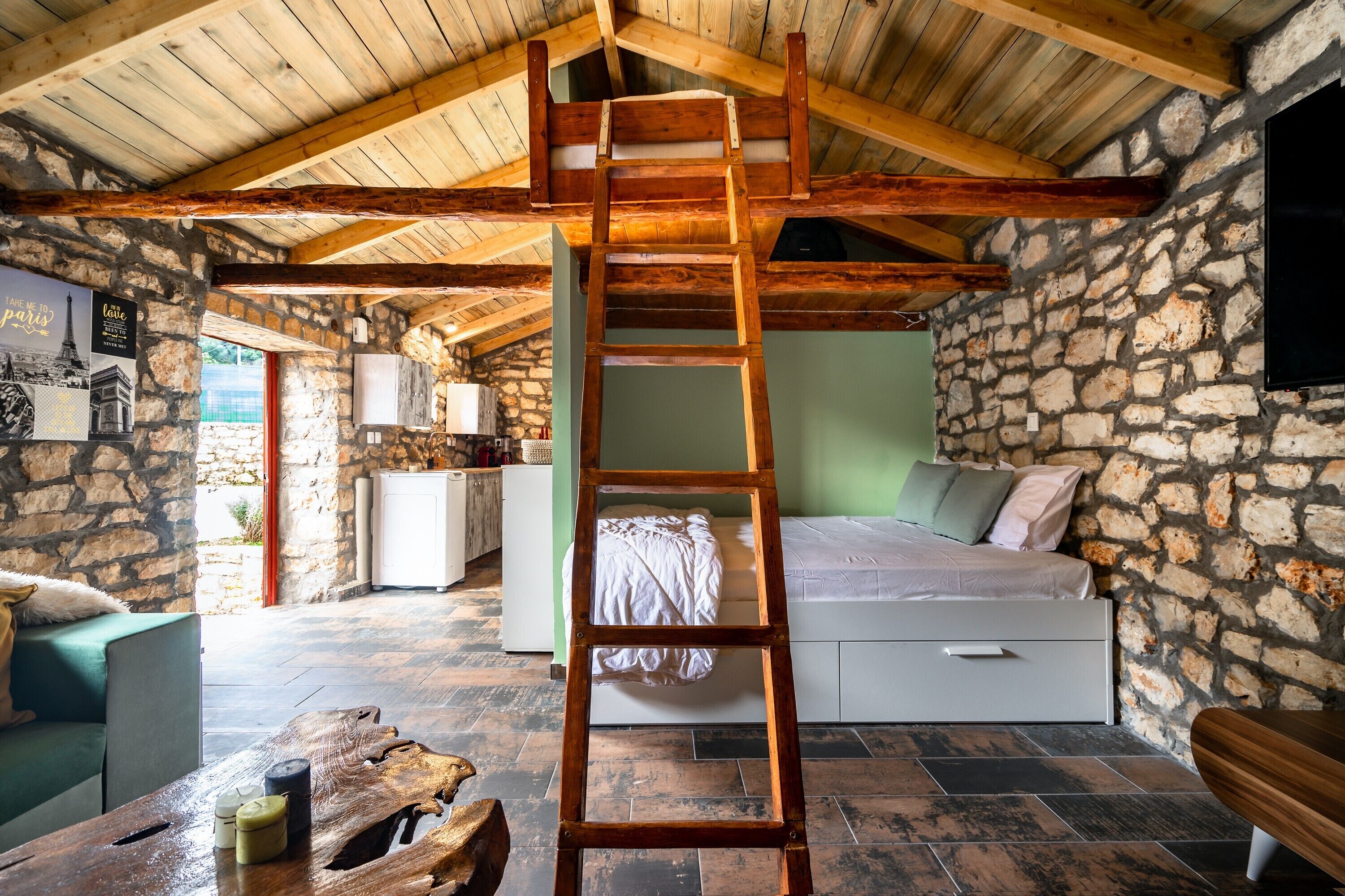 A rustic room with a wooden ladder, stone walls, a bed, a sofa, and a wooden table.
