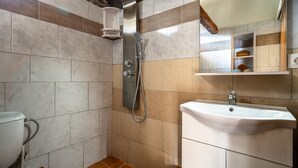 A bathroom with a shower, toilet, sink, and a mirror with a shelf above. - Villa 'Nikos' with Mountain View, Wi-Fi and Air Conditioning (KEFALONIA)