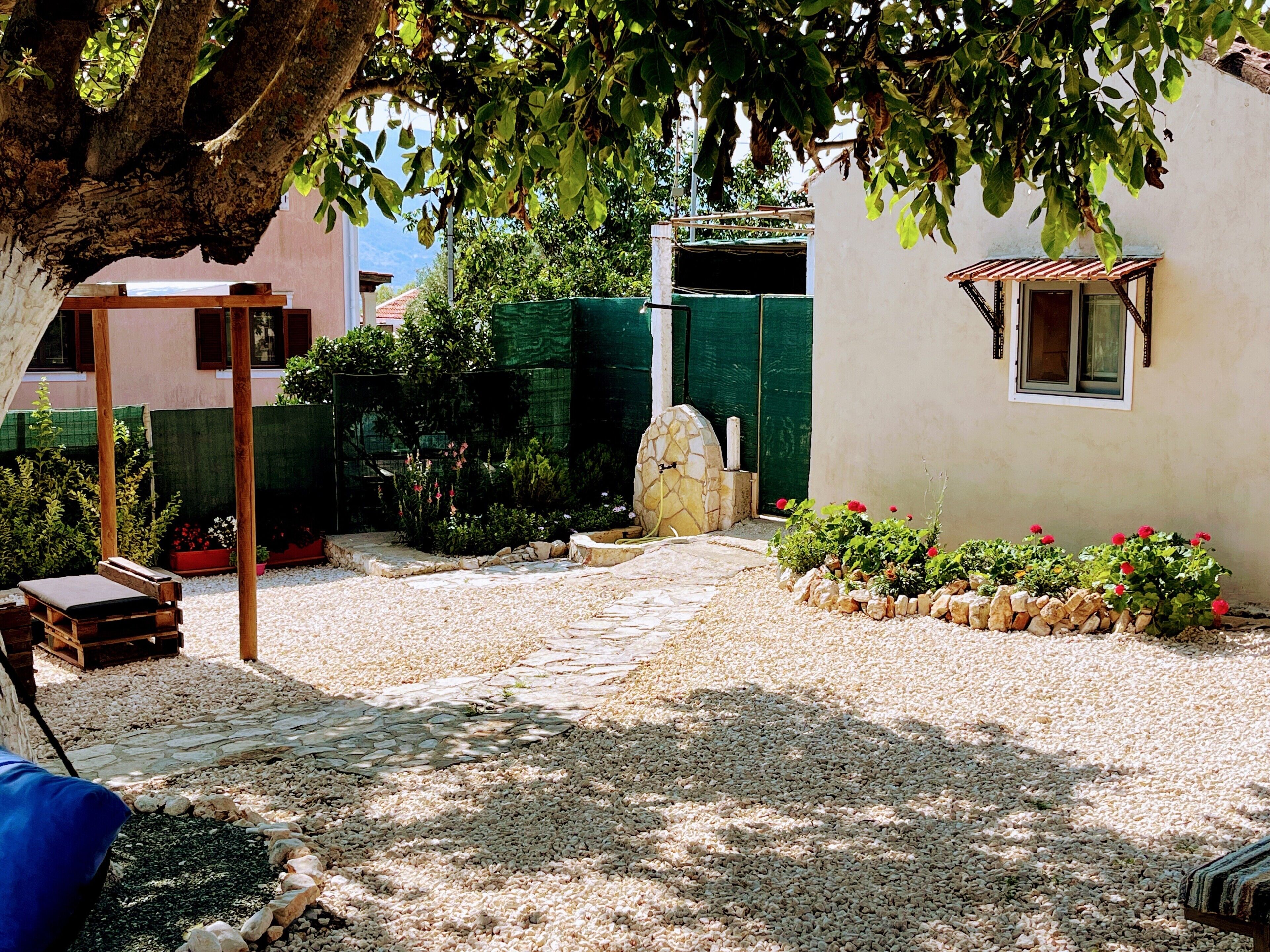 A courtyard with a stone pathway, a wooden bench, a stone structure, and a garden with red flowers.