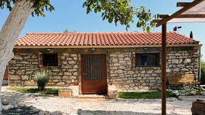 A stone building with a tiled roof, a wooden door, and a small garden area. - Villa 'Nikos' with Mountain View, Wi-Fi and Air Conditioning (KEFALONIA)
