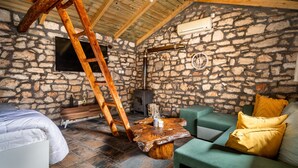 A rustic room with a stone wall, a wooden ladder, a fireplace, a green sofa, and a wooden coffee table. - Villa 'Nikos' with Mountain View, Wi-Fi and Air Conditioning (KEFALONIA)