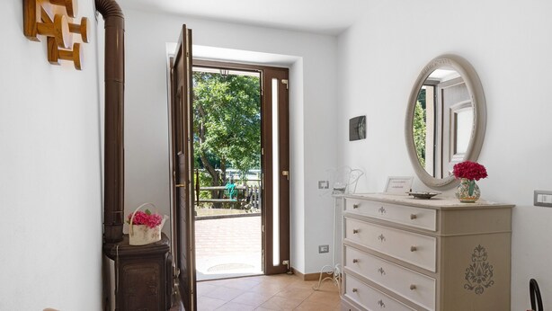 Una habitación con una silla de madera, un aparador blanco con cajones, un espejo y una puerta que da a un espacio al aire libre.