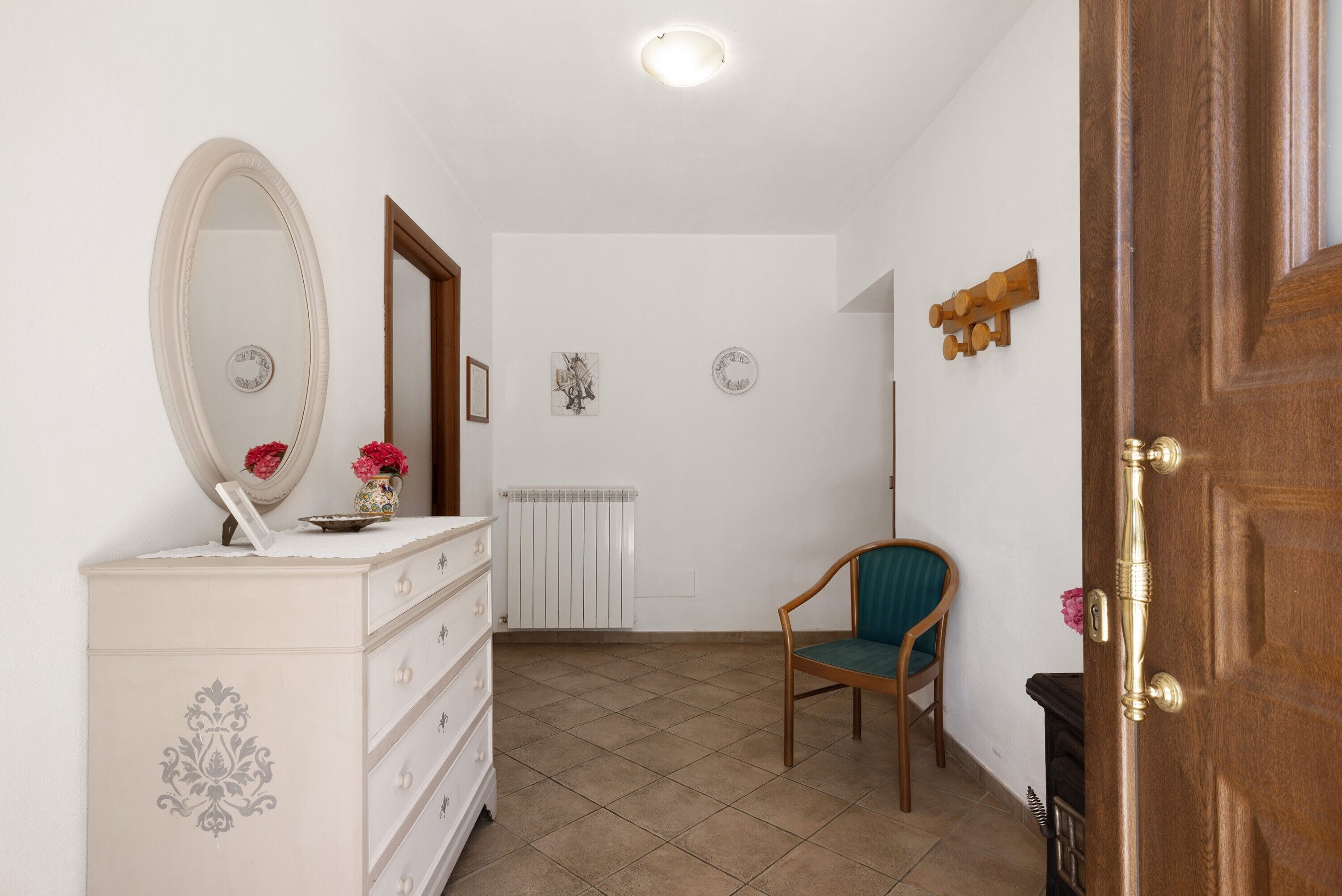 Une pièce comprenant une commode, une chaise, un miroir, un radiateur et une porte.