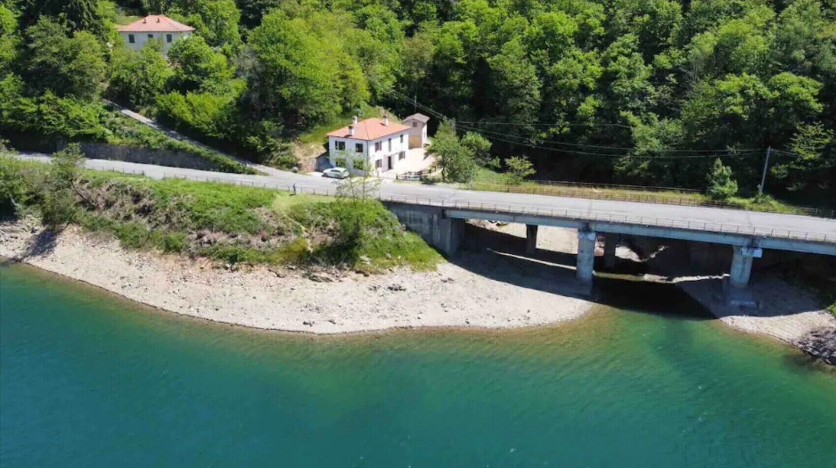 Un puente sobre un río, una casa en una ladera y abundante vegetación.