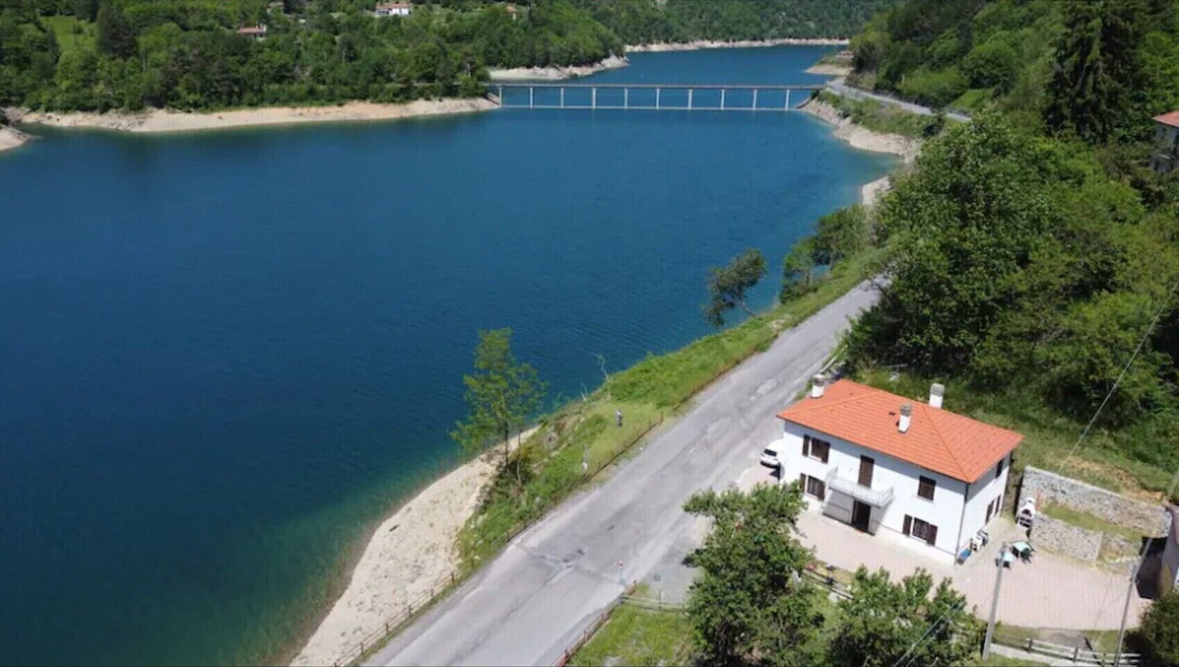 A coastal area with a bridge, a road, and a white building with a red roof.
