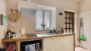 Una cocina con encimera de madera, un lavabo, una ventana con cortinas, una escoba y una puerta.