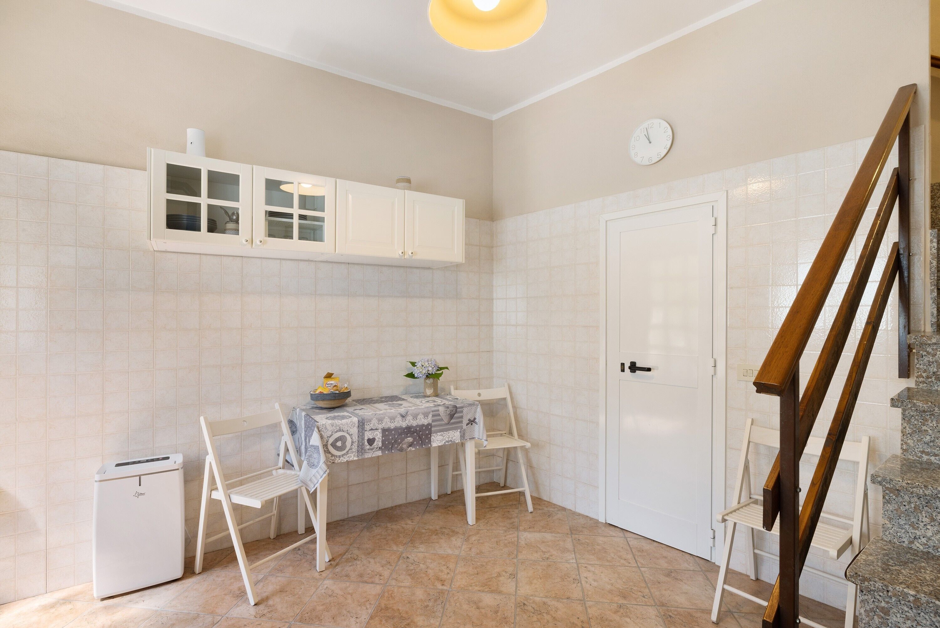 Una cocina compacta con armarios blancos, un refrigerador pequeño, una mesa de comedor con sillas y una escalera de madera.