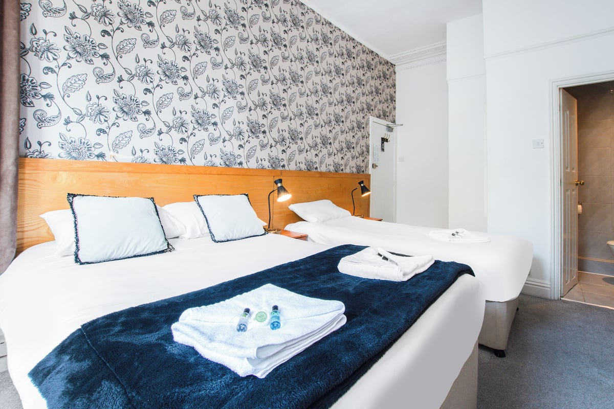 Una habitación de hotel con una cama grande, una manta azul y un cabecero con dos lámparas.