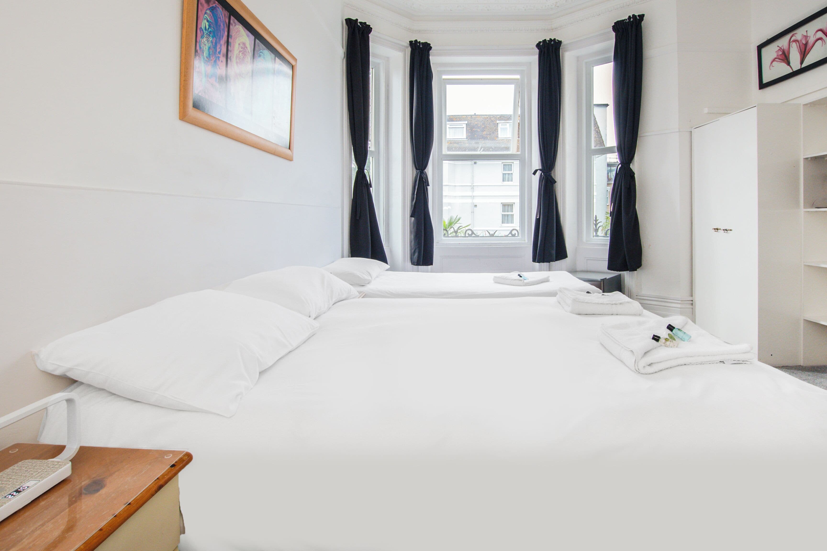 A hotel room with a large bed, a bedside table with a phone, and a window with curtains.