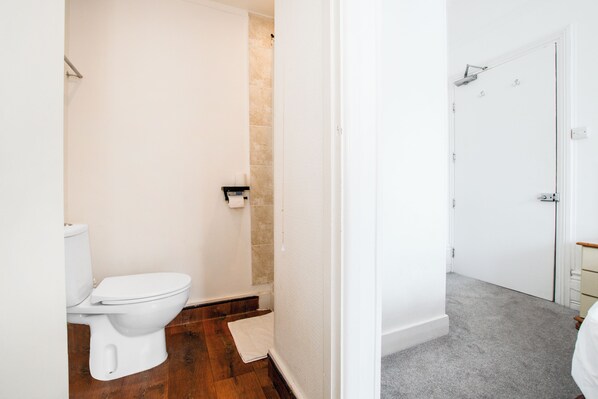 A bathroom with a toilet, a shower area, and a door leading to another room. - OYO The Lodge Bournemouth (Bournemouth)