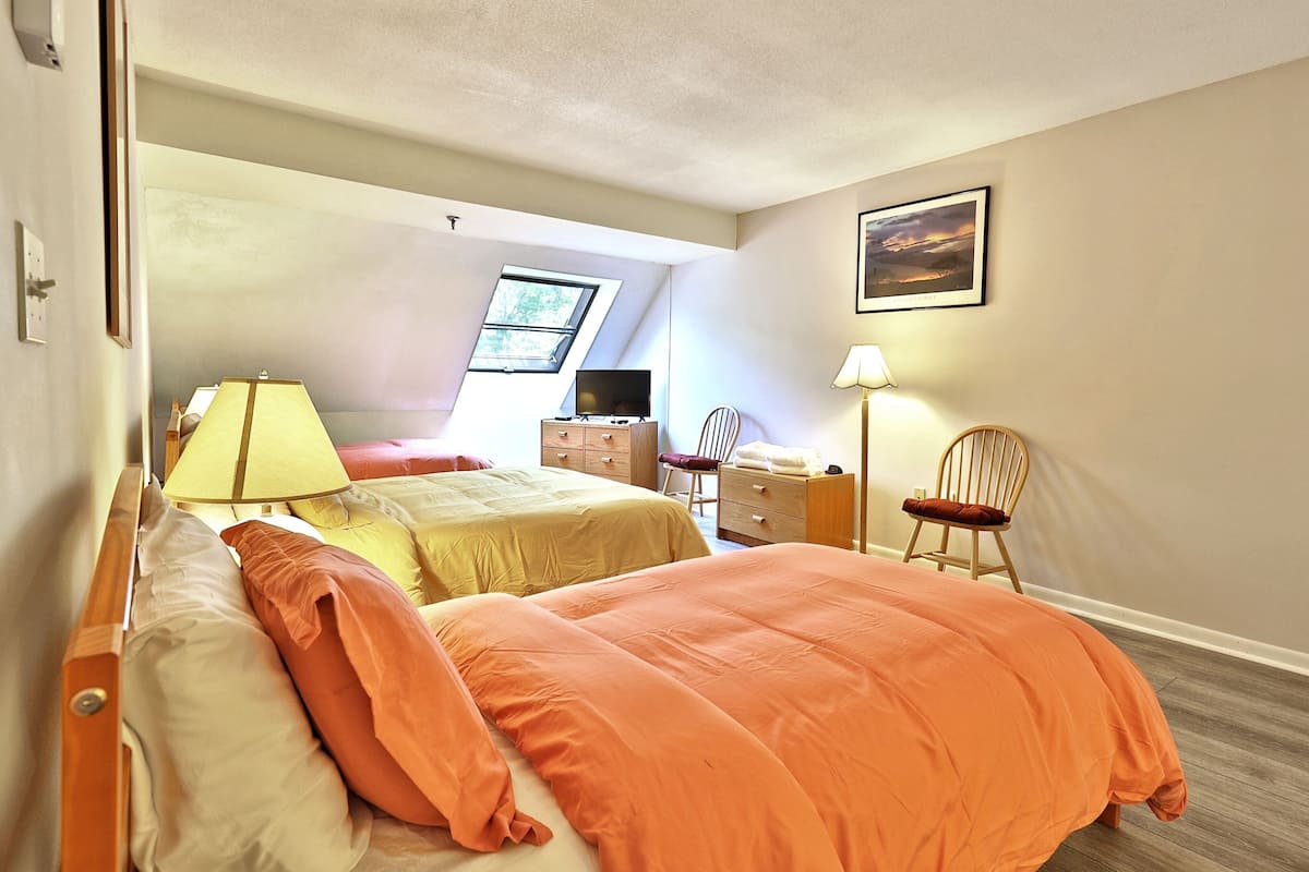 Ein Schlafzimmer mit zwei Betten, einem Schreibtisch, einem Stuhl, einer Lampe und einem Fenster.