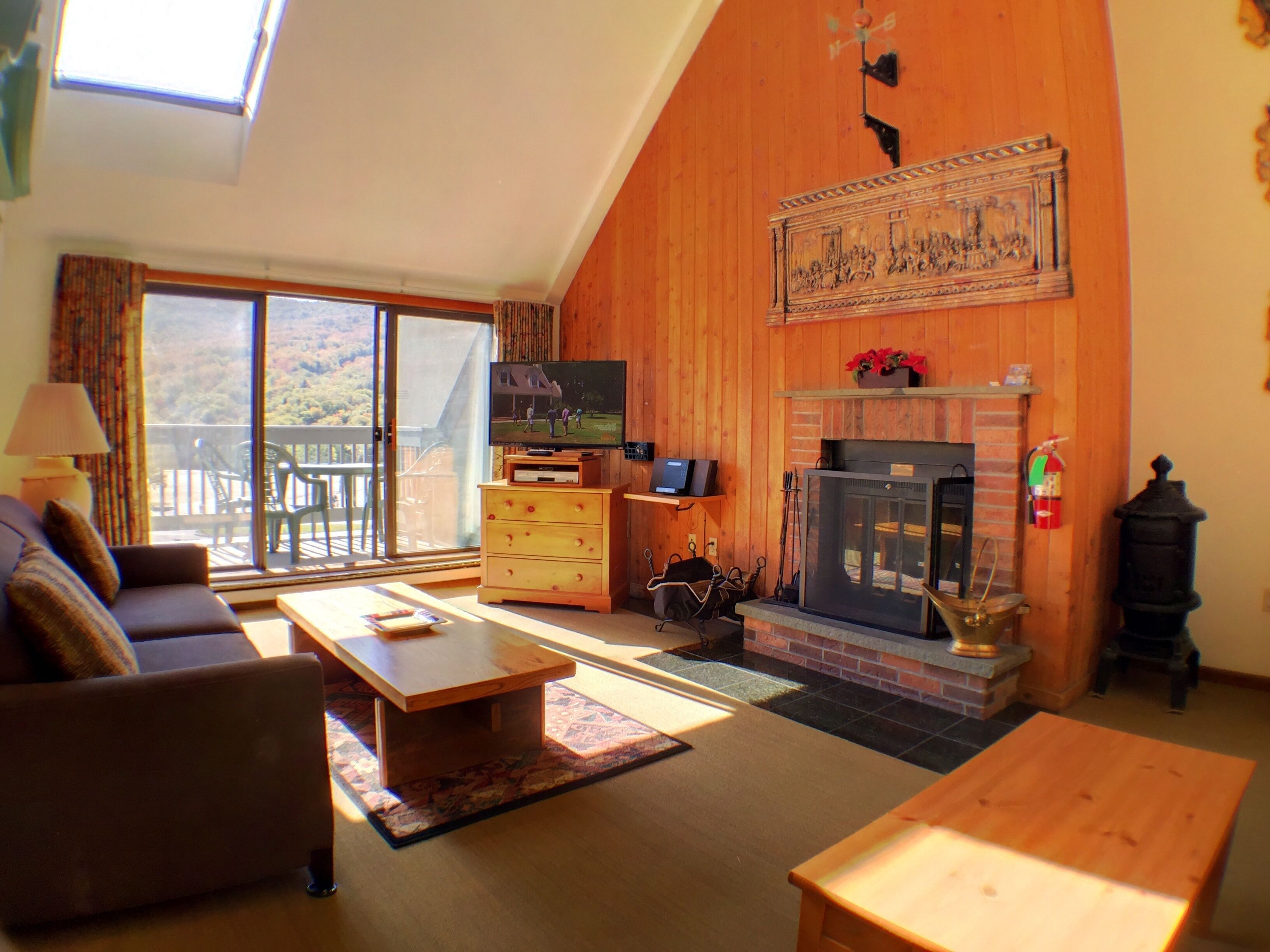 Un salon confortable avec une cheminée, un téléviseur et un balcon offrant une vue sur l’extérieur.
