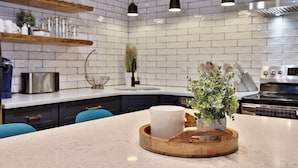 A modern kitchen with white brick walls, wooden shelves, and a central island with a white mug and a plant. - Mountain Green Resort by Killington VR - 2 Bedrooms (Killington)