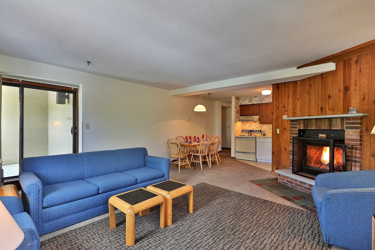Ein Wohnzimmer mit blauem Sofa, zwei Holztischen, einem Kamin und einem Essbereich mit Stühlen und Tisch.