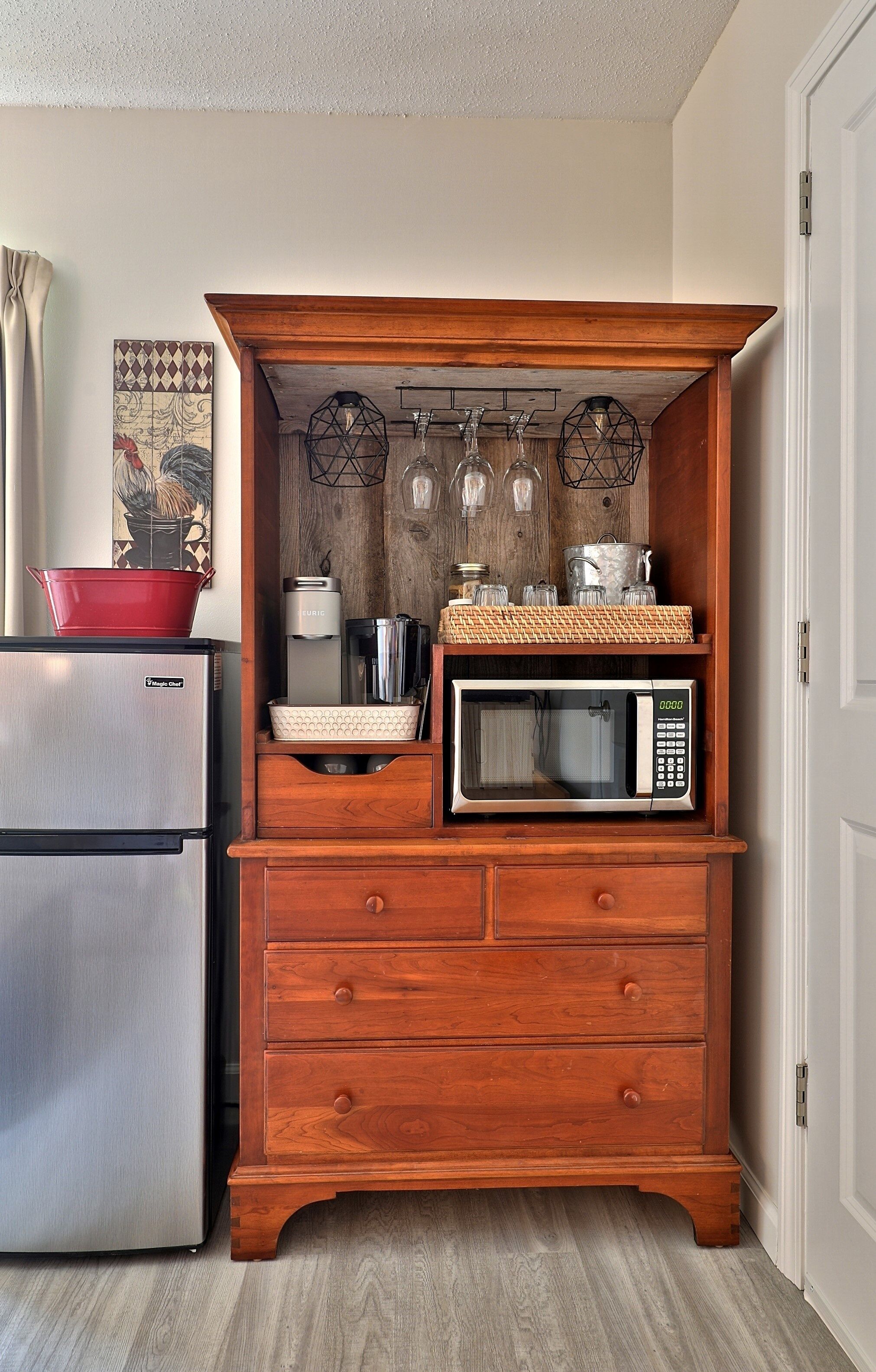 A kitchen with a wooden cabinet housing a microwave, a red pot, and a coffee maker.
