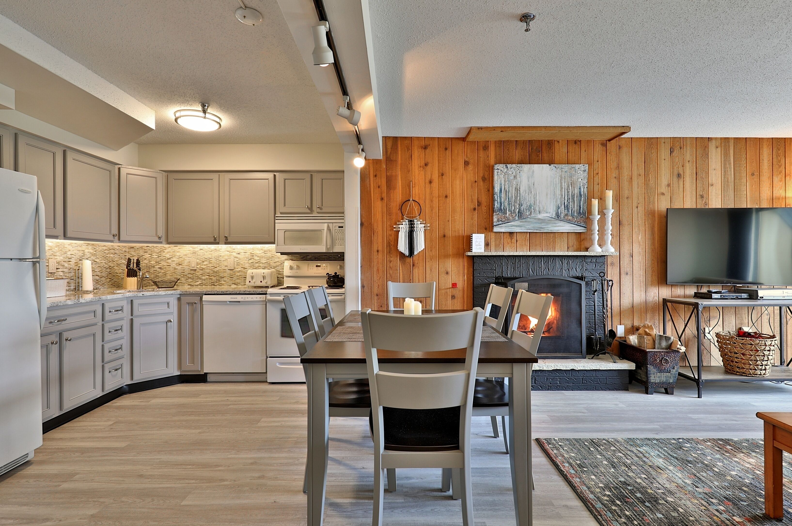 A modern kitchen with light wood cabinets, a dining area with a fireplace, and a flat-screen TV.